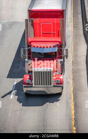 Bright red industrial diesel long haul classic big rig semi truck tractor transporting commercial cargo in covered dry van semi trailer driving on the Stock Photo