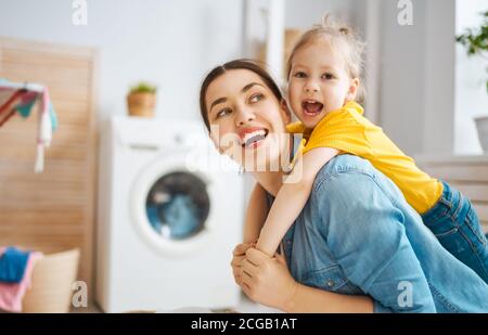 Beautiful young woman and child girl little helper are having fun and smiling while doing laundry at home. Stock Photo