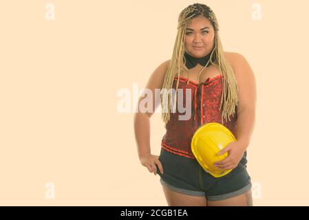 Young fat Asian construction woman holding safety helmet while posing Stock Photo