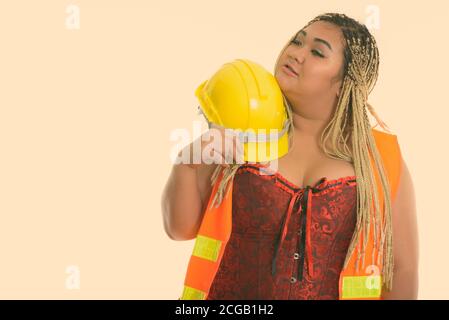 Young fat Asian construction woman holding safety helmet near the face while thinking Stock Photo