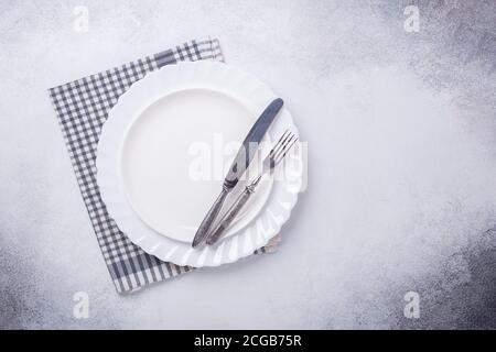 Empty white plate, linen napkin, knife and fork on stone background Copy space Top view - Image Stock Photo