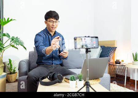 Social media influencer or blogger present and review recording or streaming vlog about product using smartphone on tripod for social media channel ma Stock Photo