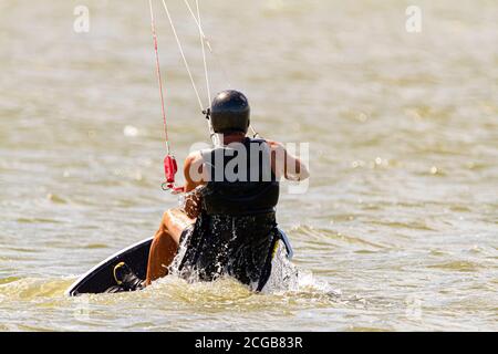A kitesurfer wearing protective equipment is losing balance and falling off the board into the sea off the coast of Assateague Island.. He then finds Stock Photo