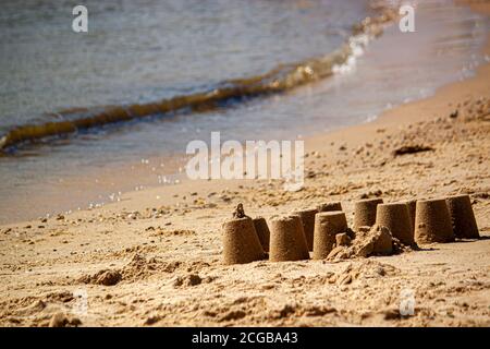 An abstract beach holiday themed image featuring a close up look to a sand castle made with wet sand on a beach. There is nobody and calm sea is in th Stock Photo