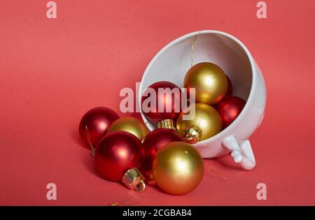 Red and gold Christmas balls lie in a white ceramic mug on a red background Stock Photo