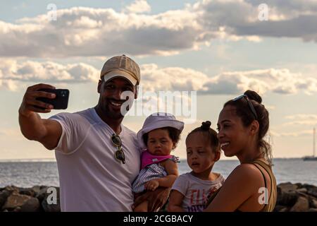 Rock Hall, M, USA, 08/30/2020: A young and happy African American family is taking a selfie at the beach by the Chesapeake Bay. The parents hold their