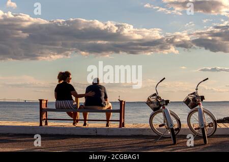 Rock Hall, MD, USA 08/30/2020: A middle aged caucasian couple is sitting on a bench by the beach. They have their identical bikes parked next to them. Stock Photo