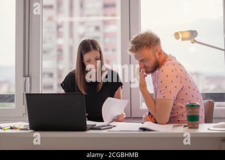 two young people studying together or discussing new business project, looking at papers. Stock Photo