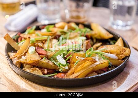 Fried potatoes with sausage on a black cast-iron pan in a restaurant. Stock Photo