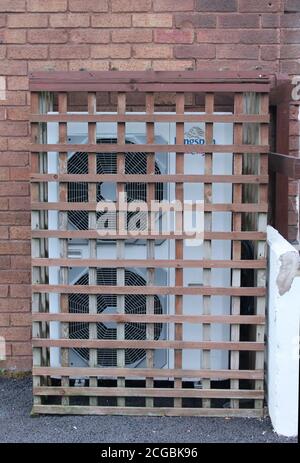 Air conditioning unit located on brick wall of a building encased in wooden trellis Stock Photo