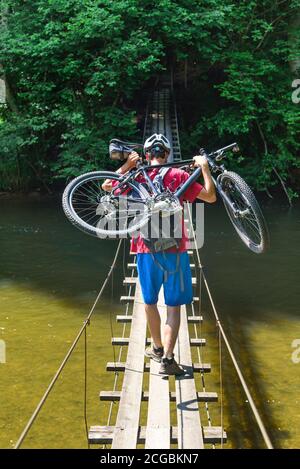 A cyclist carries his bike over a narrow suspension bridge over the Wertach in Allgäu