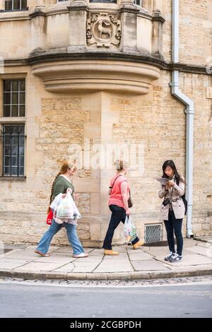 Asian woman tourist staying still reading a guide book on Catte street in Oxford Oxforshire while local people passing by Stock Photo