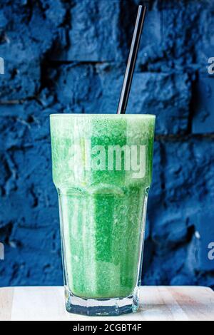 Green smoothie made from herbs and vegetables in a large glass glass against a dark stone wall Stock Photo