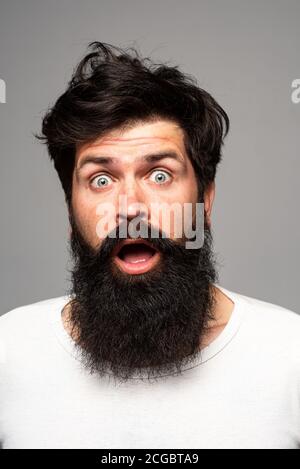 Surprised handsome man. Shocked male model with surprise expression, wow amazed excited face. Barber with long beard and moustache in barbershop Stock Photo