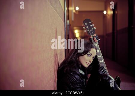 Young woman singer with guitar portrait in corridor interior Stock Photo