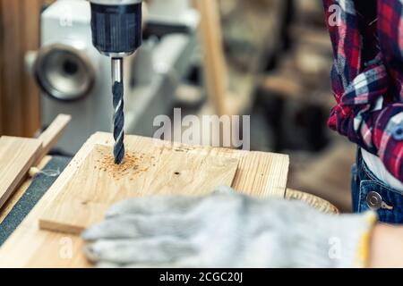 Closeup view professional carpenter hand making hole with electric drill in wood plank in carpentry diy workshop. Detail of furniture diy restoration Stock Photo