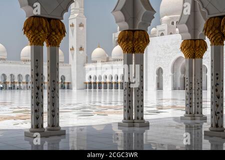 A day shot from the archway inside the  Sheikh Zayed Grand Mosque, Abu Dhabi looking into the inner courtyard. Architectural features of marble columns with date palm capitals, arches, domes and a minaret. Mosque completed 2007. Stock Photo