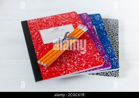 Bundle of wood pencils tied with black and white bow laying on group of colorful composition books on white wood table background. Stock Photo