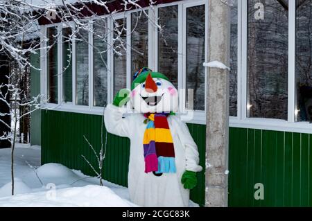 A snowman in a costume near a wooden building. Cristmas. Stock Photo