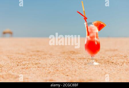 red grapefruit cocktail with juice on sandy beach line at seascape on horizon Stock Photo