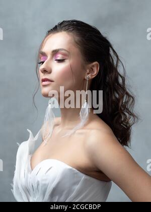 Stylish and elegant bride in a modern suit, portrait. Makeup in shades of pink, drop earrings with white feathers. Stock Photo