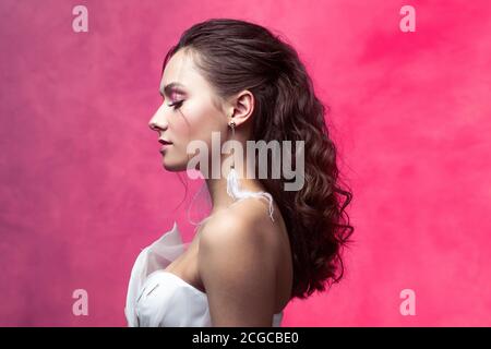 Portrait of a young beautiful woman in elegant white, textured pink background. The bride with a light and stylish styling. Beautiful young brunette, Stock Photo