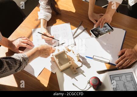 Close up hands of architect-engineer and young couple during presentation of future house. Top view table with documents, blueprint. First home, industrial, building concept. Moving to new live place. Stock Photo