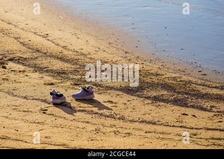 Pair of chabby abandoned sneakers on a sandy yellow lonely beach near water Stock Photo