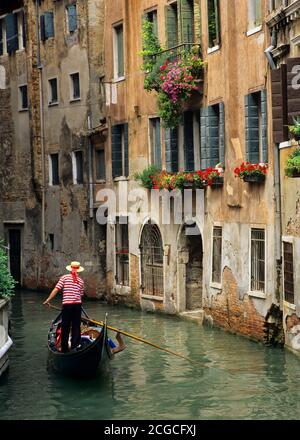 Gondola and Gondolier and flower-filled window boxes on side canal in Venice Stock Photo