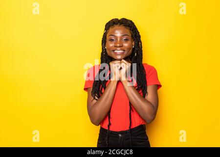 Beautiful african woman arms touch cheekbones look wondered empty space charming toothy smile isolated on yellow background Stock Photo