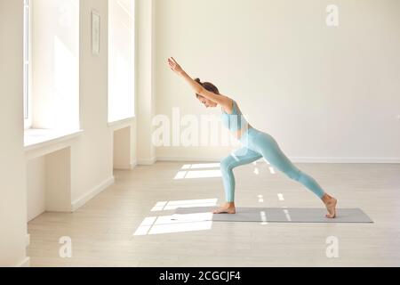 Serious young woman practicing balancing asana standing on rubber mat during yoga workout in gym Stock Photo