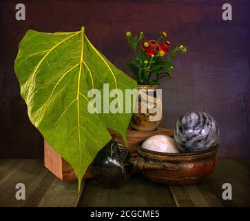 A small bouquet in a vase and a large green leaf on a wooden stand. Marble balls in a copper dish. Still life. Vintage. Stock Photo