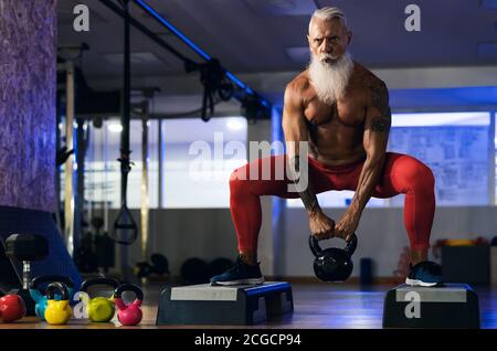 Senior fitness man doing kettle bell exercises inside gym - Fit