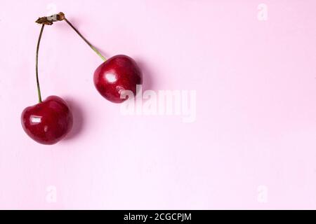 Red berries of tasty juicy cherry lie on pink in the left upper corner. Photo flat lay on pink background with free space Stock Photo