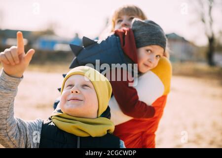 Caucasian Boy Of 6-7 Years Looking At Flying Kite With Mom And Little Brother. Pleasant Activity In Fresh Air On A Sunny Spring Or Autumn Day Stock Photo