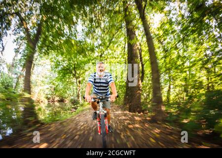 Senior man going fast on his bike during his regular afternoon ride - enjoying actively his retirement - motion blur used to convey speed and movement Stock Photo