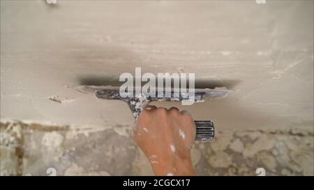 construction notched trowel and worker hands with white mortar on wall. Worker levels a wall with mortar Stock Photo