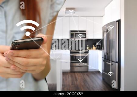 A woman controls home appliances. Kitchen automation. IoT, Internet of things. A woman controls the kitchen appliances with the smartphone. Stock Photo
