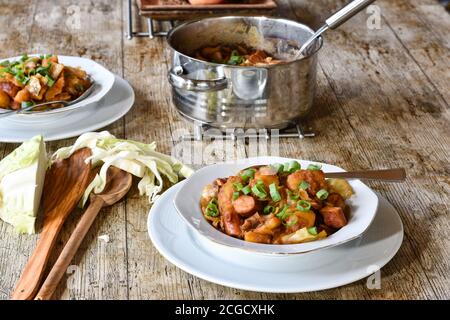 2 white plates of vienna potato goulash / stew served on a wooden rustic table with soup pot for dinner Stock Photo