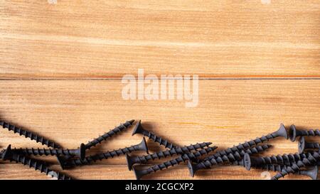 Self-cutters on a wood brown background banner with space for text. Construction tools, self-tapping screws for fastening. Black screw hardware Stock Photo