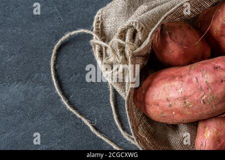 A heap of raw sweet potatoes in a jute bag on black background Stock Photo