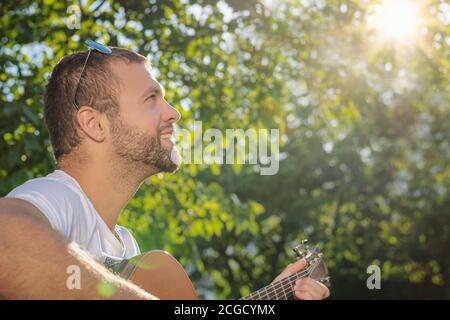 Summertime in garden. Young man is playing acoustic guitar in the garden at sunset. Stock Photo