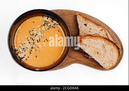 Traditional autumn vegetable soup with pumpkin and sesame seeds and two slices of toasted bread on wooden board top view Stock Photo