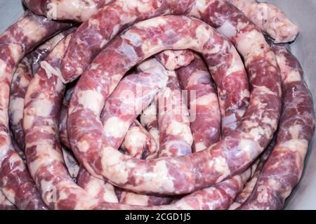 Making homemade sausage at home. Stuffing pork intestine with meat and fat. The photo shows the stage when the already stuffed raw sausage is rolled i Stock Photo