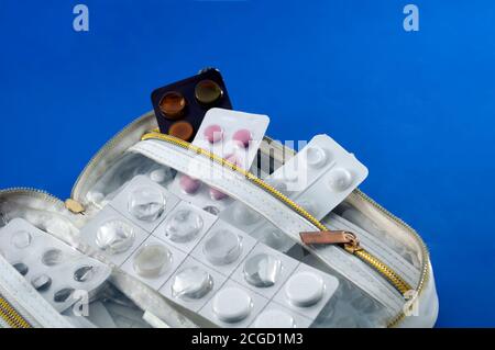 White handbag, with half-empty tablet blisters on blue background, Stock Photo