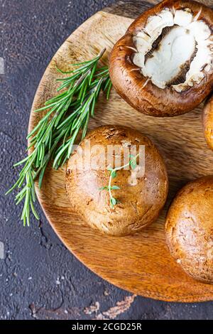 Fresh delicious portobello mushrooms with thyme and rosemary on wooden cutting board, dark stone background. Top view. Stock Photo