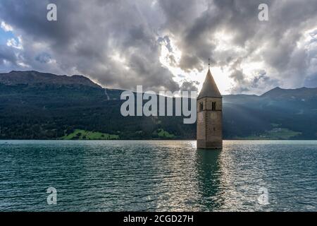 The sun sets behind the famous submerged bell tower in Lake Resia, Curon Venosta, South Tyrol, Italy Stock Photo