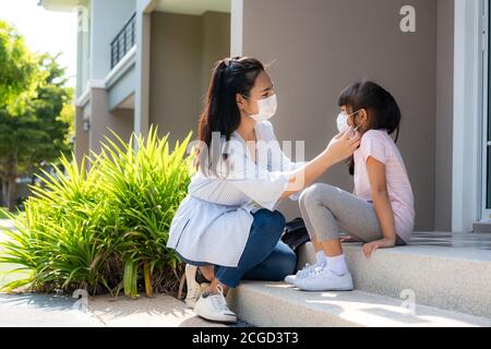 Asian mother help her daughter wearing medical mask for protection Covid-19 or coronavirus outbreak in village park to prepare go to school when back Stock Photo