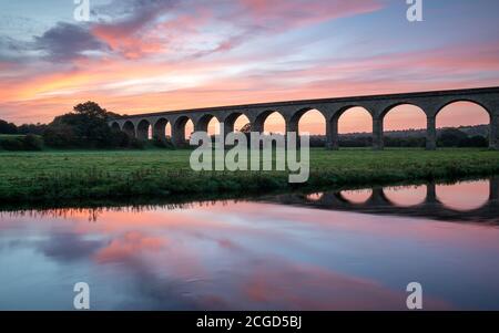 Arthington Viaduct is reflected in the River Wharfe during a colourful sunrise, the vibrant coulours in the sky mirrored by the water. Stock Photo