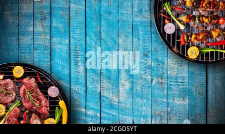 Top view of fresh beef steaks, skewers and vegetable on grills placed on wooden floor. Barbecue, grill and food concept Stock Photo